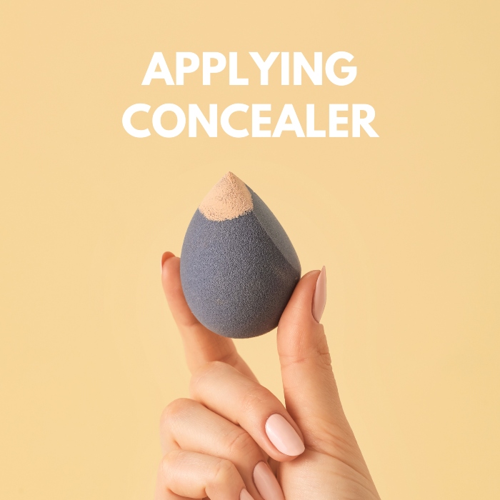 Grey base maker sponge with concealer in a hand